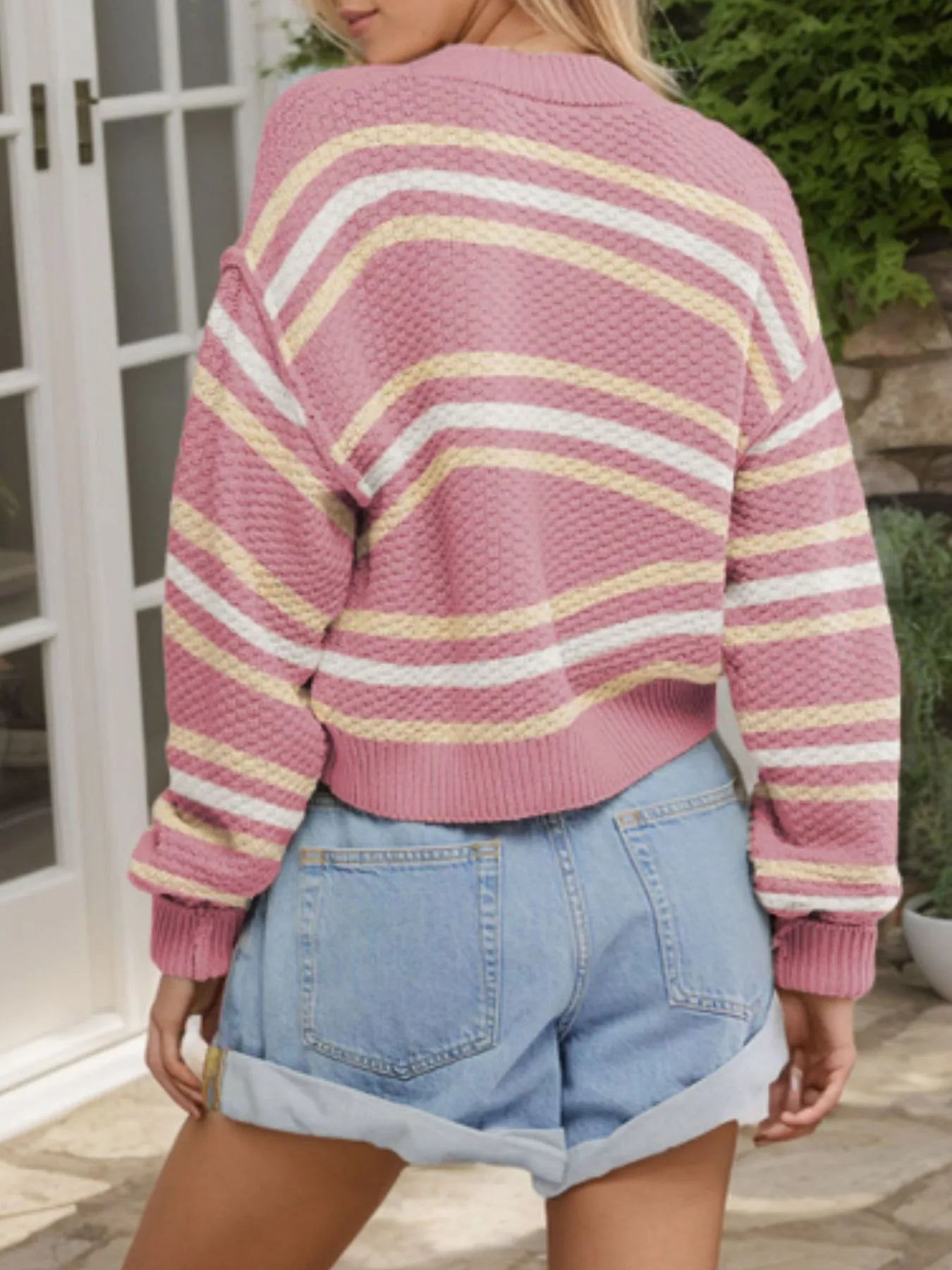 Person wearing a pink and yellow striped sweater with denim shorts outdoors.