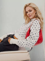 Woman sitting on a chair wearing a white sweater with black patterns and holding a red handbag.