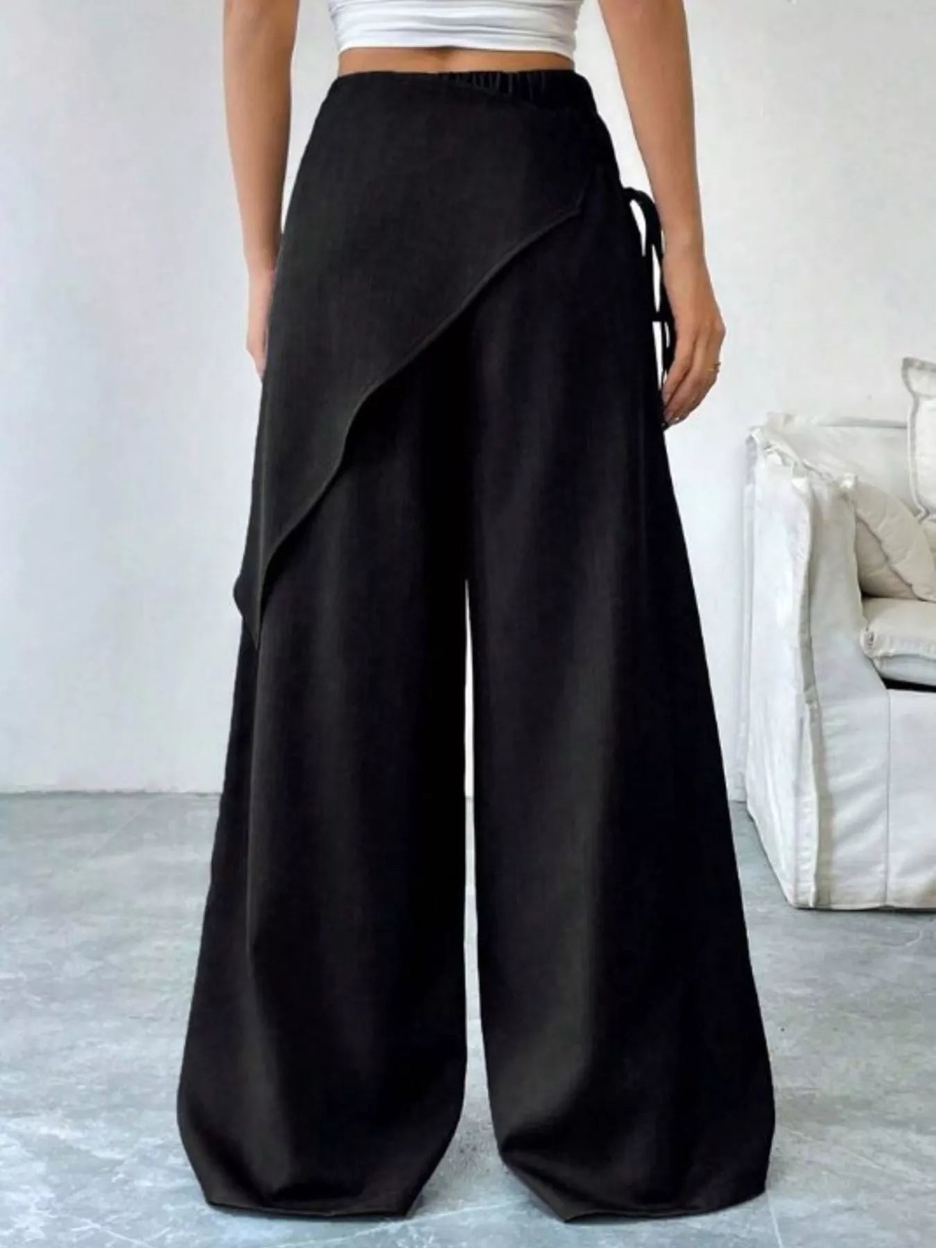Person wearing black wide-leg pants with a white top in a minimal indoor setting.