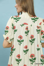 Woman wearing a cream dress with floral pattern against a blue background