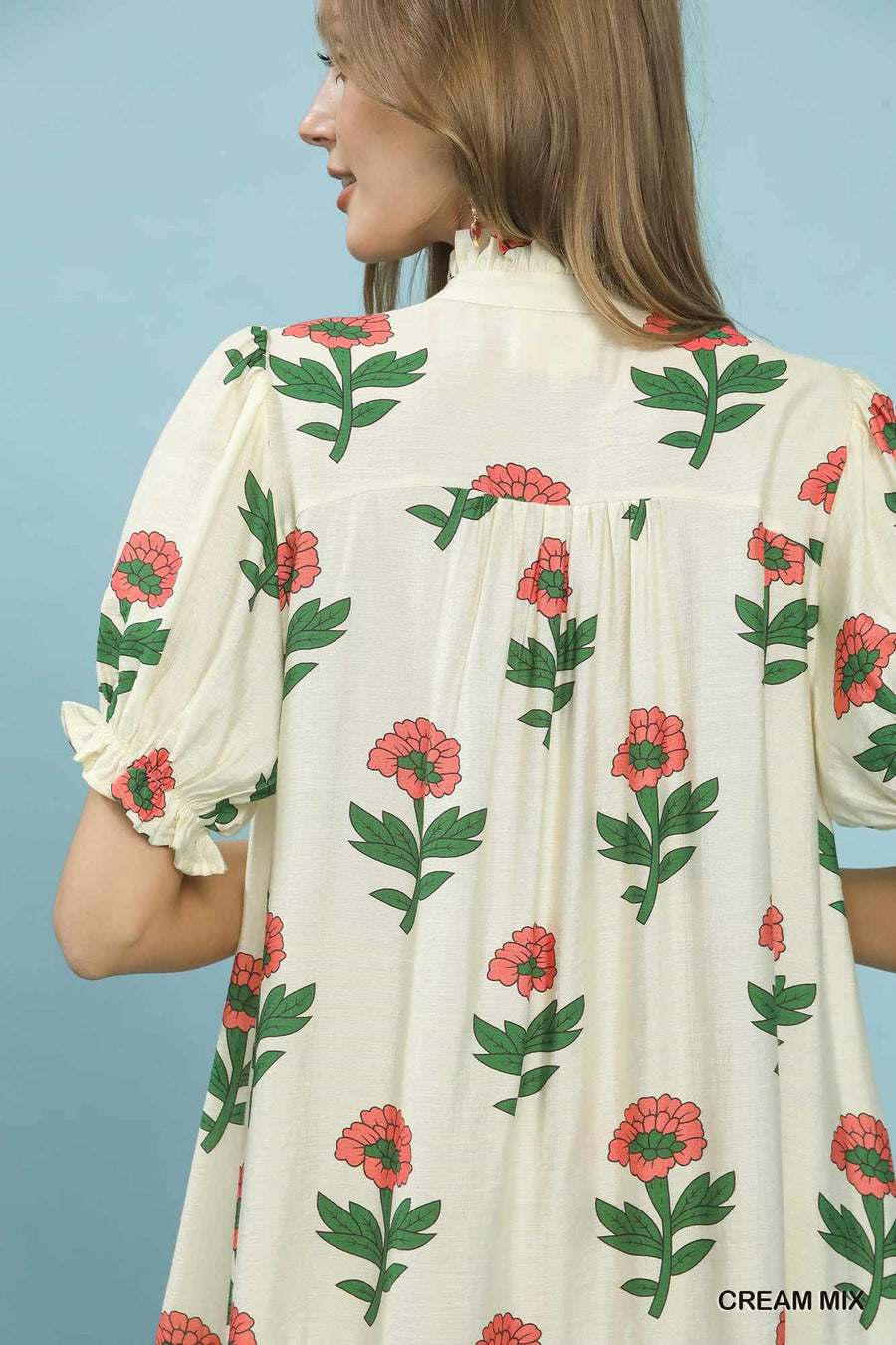 Woman wearing a cream dress with floral pattern against a blue background