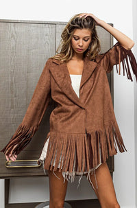 Woman wearing a brown fringed jacket and skirt against a neutral background