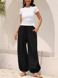 Woman wearing a white t-shirt and black wide-leg pants standing against a light-colored wall.