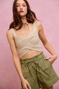 Woman wearing a beige knitted top and green shorts against a pink background