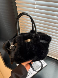 Black fur handbag held in front of a window with blinds.