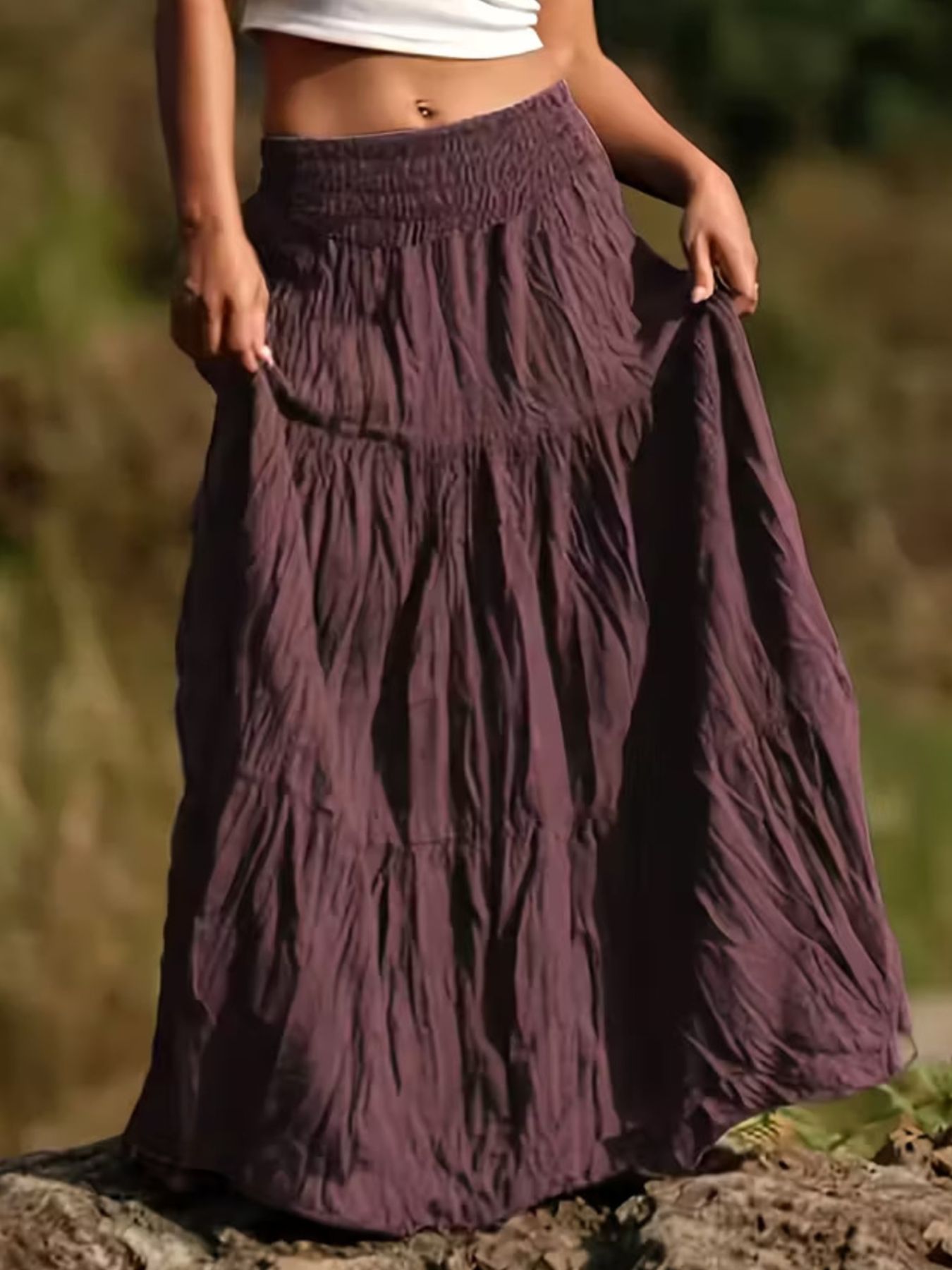 Person wearing a long, tiered purple skirt with a blurred natural background