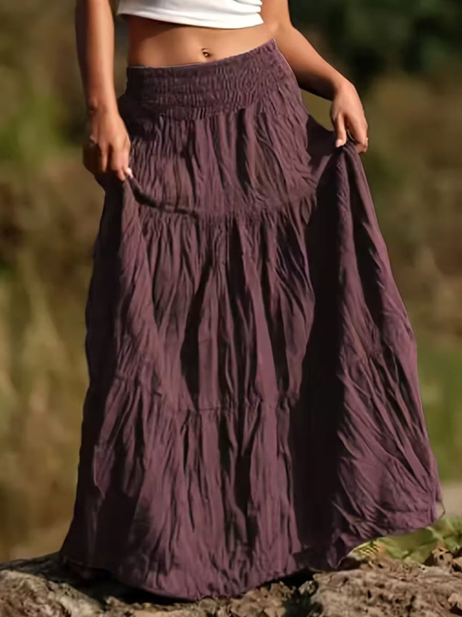 Person wearing a long, tiered purple skirt with a blurred natural background