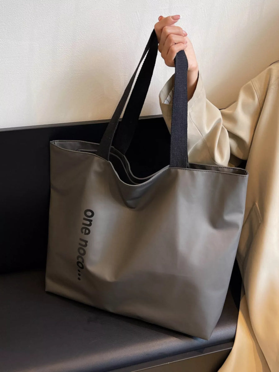 Person holding a gray tote bag with 'one new' branding on a light background