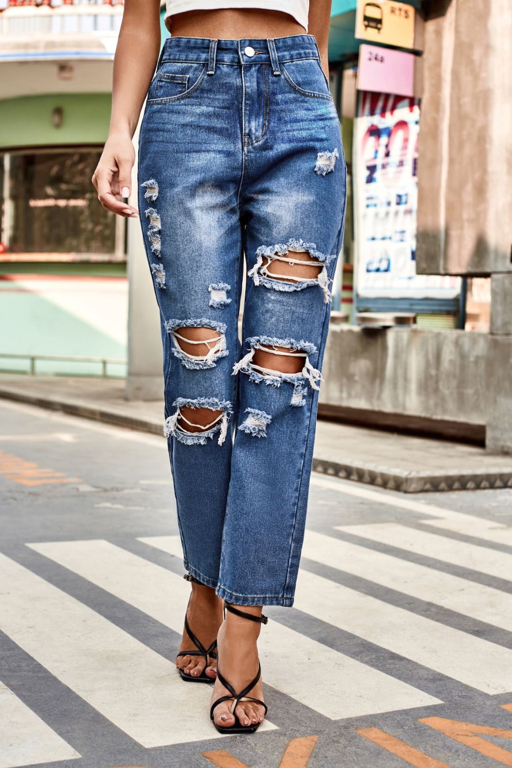 Person wearing ripped blue jeans on a city street.