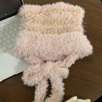 Fluffy pink scarf with a bow on a wooden surface next to a laptop.
