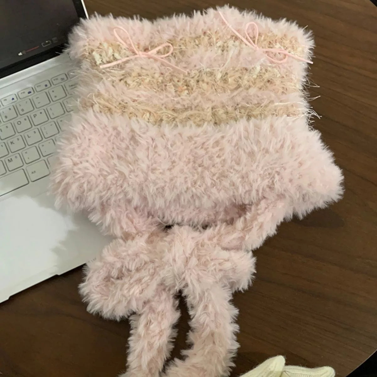 Fluffy pink scarf with a bow on a wooden surface next to a laptop.