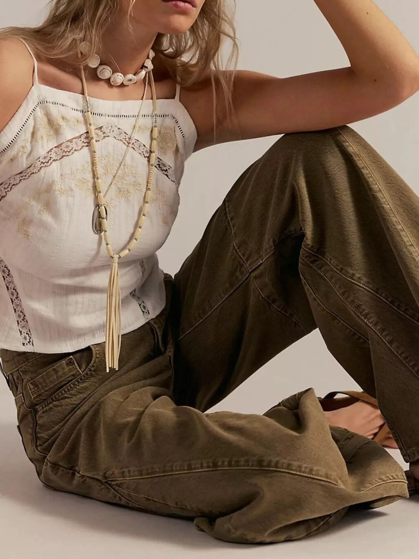 Person wearing a white lace top and brown pants sitting on a light background