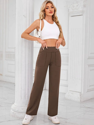 Woman wearing a white crop top and brown high-waisted pants in an elegant interior setting.