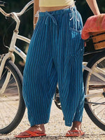 Person wearing blue harem pants standing next to a bicycle on a street.