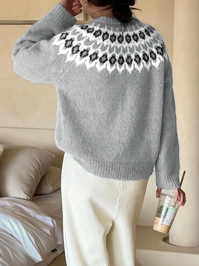 Person wearing a gray sweater with a floral pattern on the back, standing in a room.