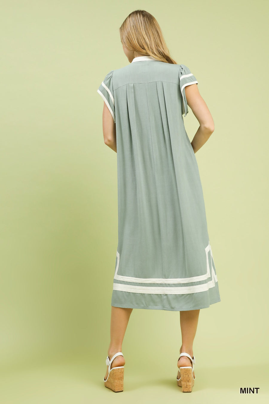 Woman wearing a light green dress with white accents on a solid background