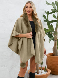 Woman wearing a green poncho with fur trim standing next to a potted plant.