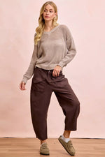 Woman wearing a beige sweater and brown pants against a pink background