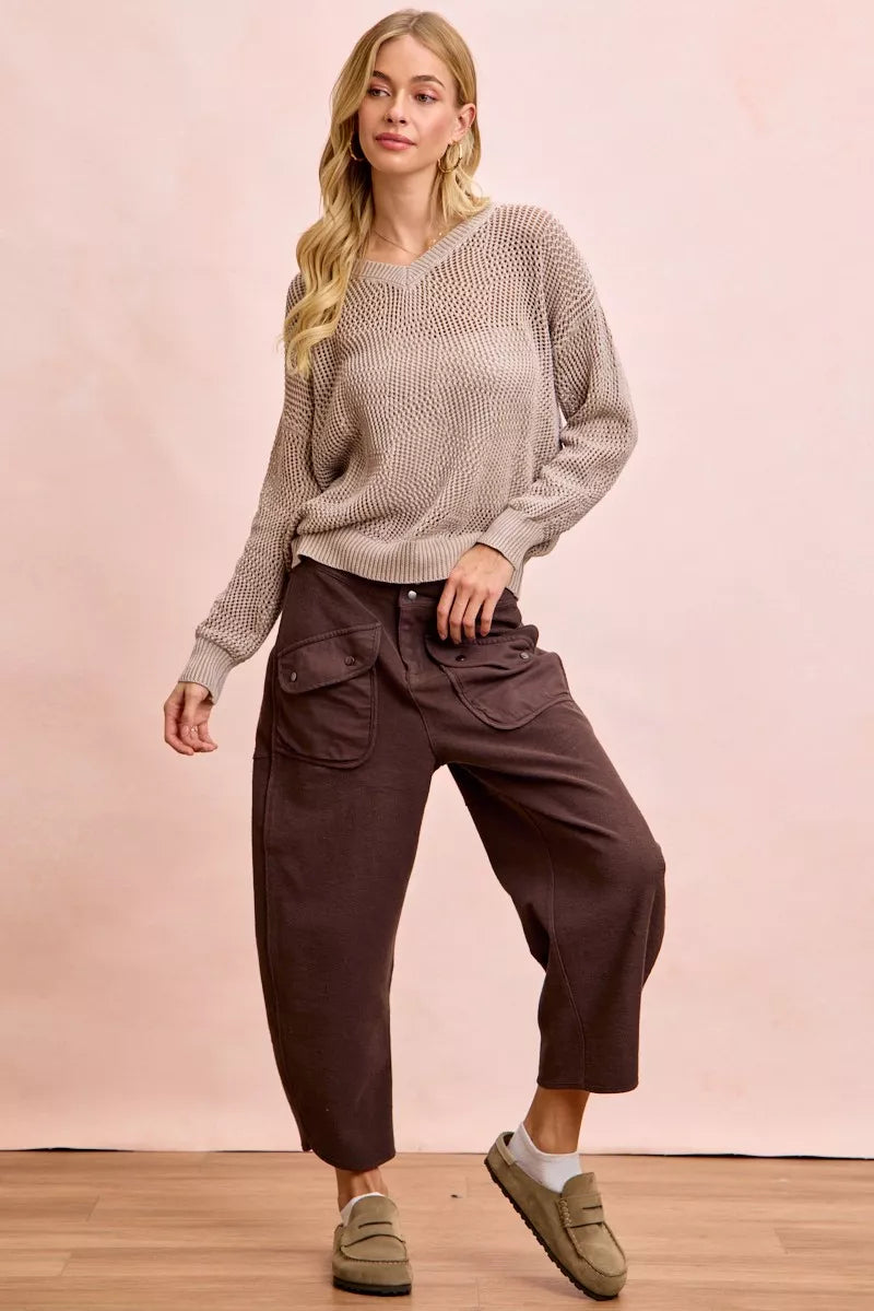 Woman wearing a beige sweater and brown pants against a pink background