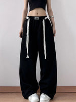 Person wearing black wide-leg pants with white drawstrings on a plain background