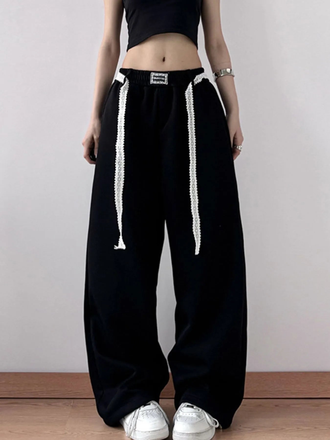 Person wearing black wide-leg pants with white drawstrings on a plain background