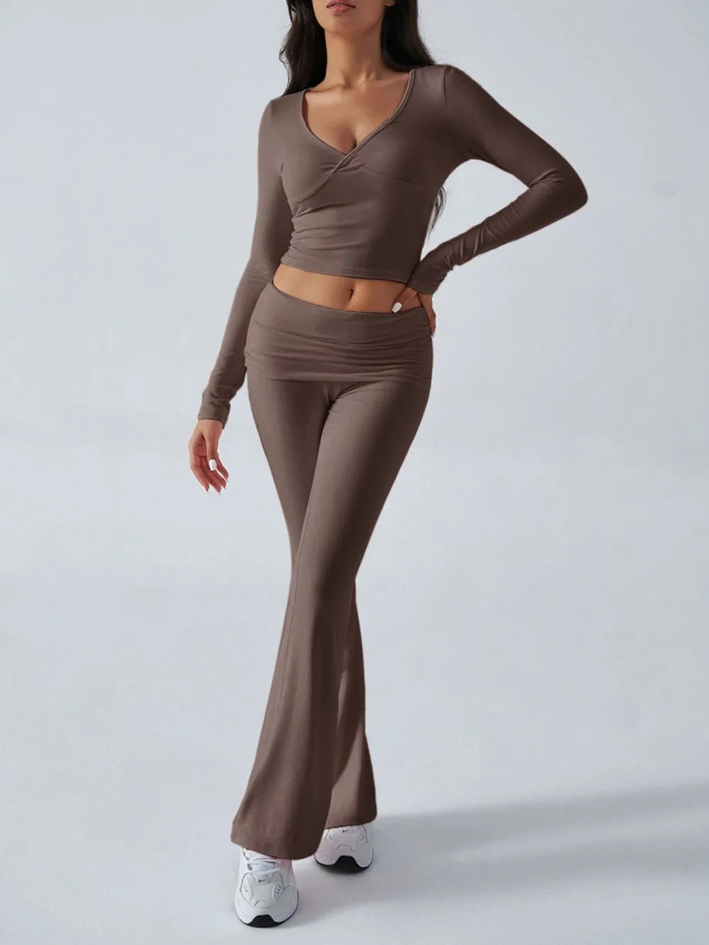 Woman wearing a brown long-sleeve top and flared pants on a white background