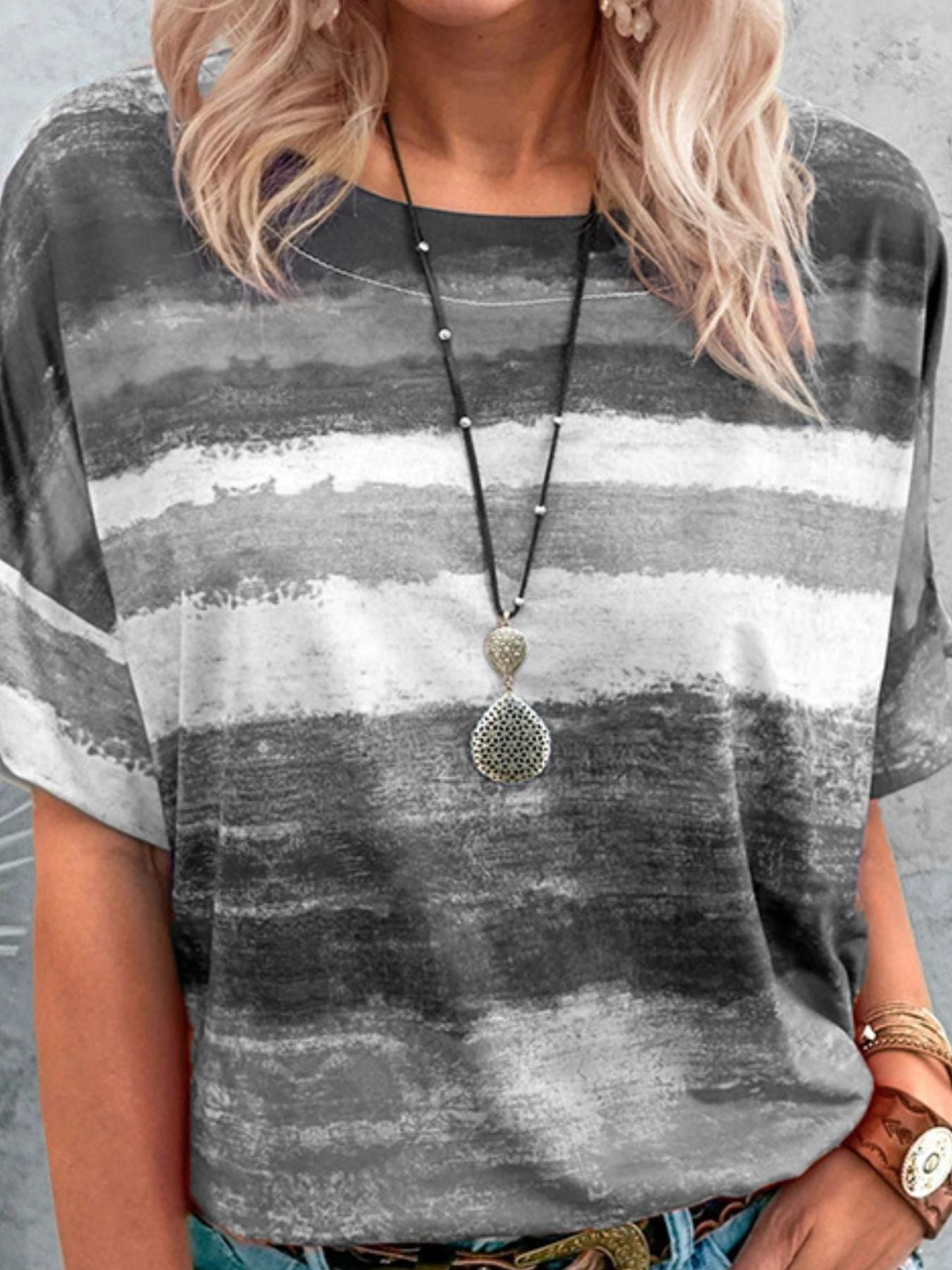 Person wearing a gray and white striped shirt with a necklace.