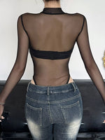 Person wearing a sheer top and jeans with a neutral background