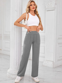 Woman wearing a white crop top and gray high-waisted pants in an elegant interior setting.