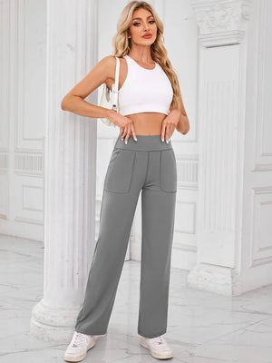 Woman wearing a white crop top and gray high-waisted pants in an elegant interior setting.