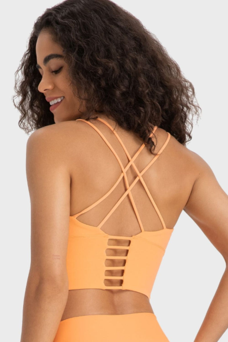 Woman wearing an orange sports bra and leggings with criss-cross back design on a white background
