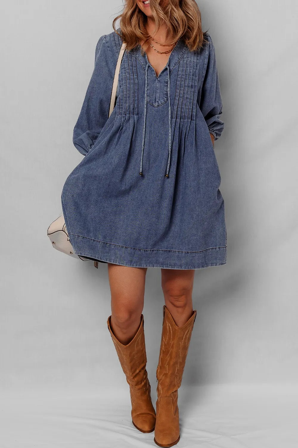 Woman wearing a blue denim dress with brown knee-high boots on a plain background