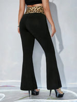 Person wearing black flared pants with a leopard print belt on a white background