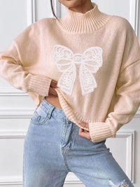 Beige sweater with a butterfly design worn by a person, against a white wall.