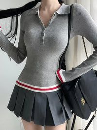 Person wearing a gray ribbed sweater and pleated skirt with a black bag.