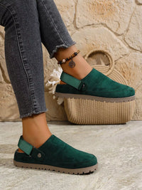 Green suede clogs worn with gray jeans against a stone wall background