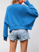 Person wearing a blue sweater and denim shorts on a plain background