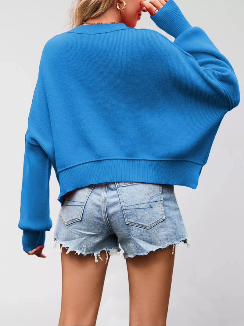 Person wearing a blue sweater and denim shorts on a plain background