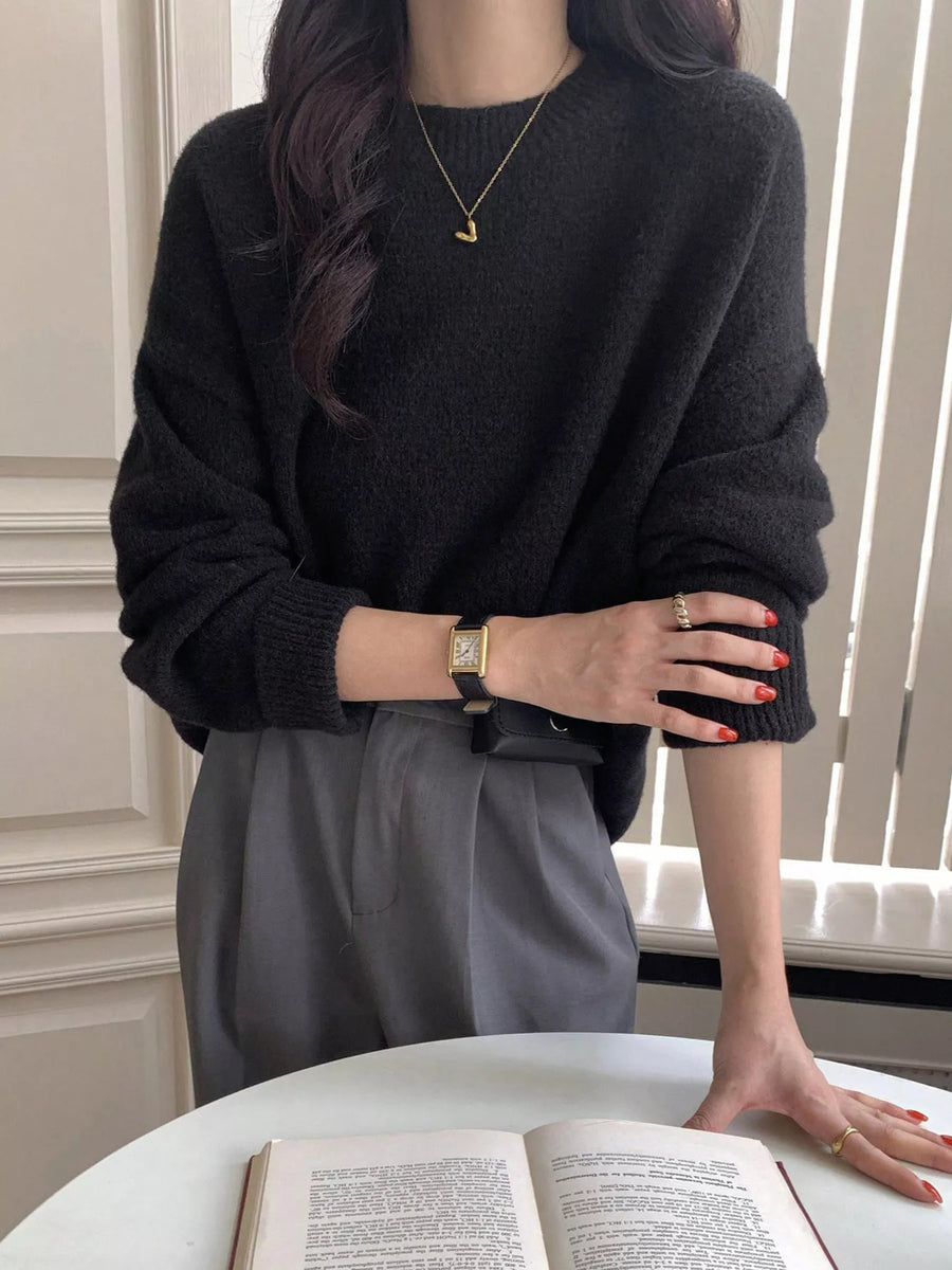 Person wearing a black sweater and gray pants, holding an open book.
