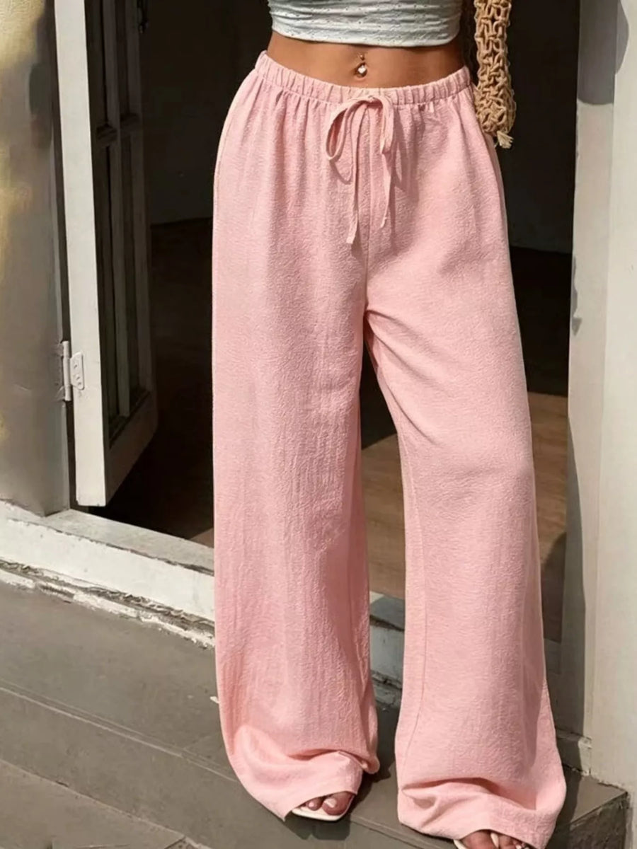 Person wearing pink wide-leg pants standing on a wooden deck.