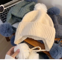 White knit hat with pom-pom held by a hand on a laptop keyboard.