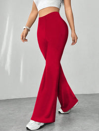 Person wearing red flared pants and white top on a plain background