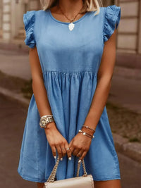 Woman wearing a blue dress holding a beige handbag with a blurred background