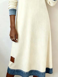 White dress with blue hem and cuffs worn by a person on a plain background
