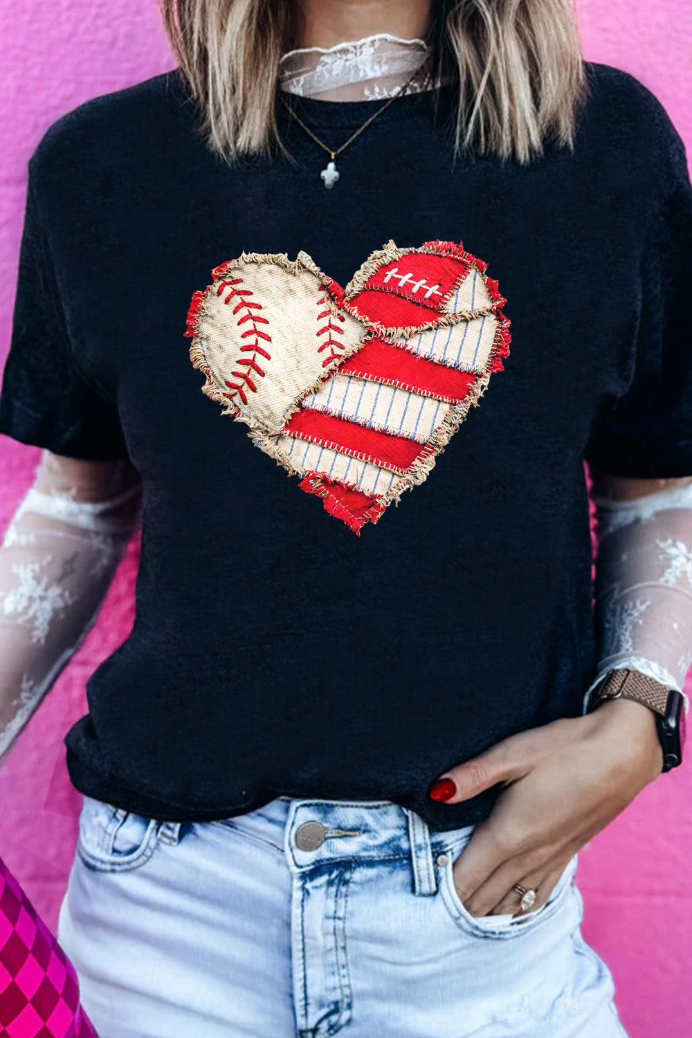 Person wearing a black t-shirt with a heart design made of baseball and American football elements on a pink background.