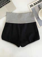 Black shorts with gray waistband on a white surface with a laptop and magazine in the background.