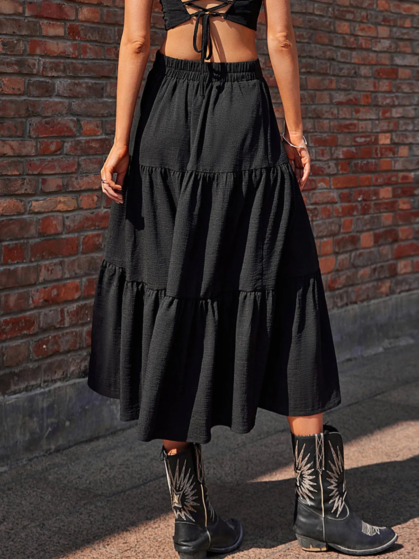 Person wearing a black tiered skirt and cowboy boots against a brick wall.