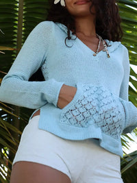 Woman wearing a light blue knitted sweater with lace details against a green leafy background