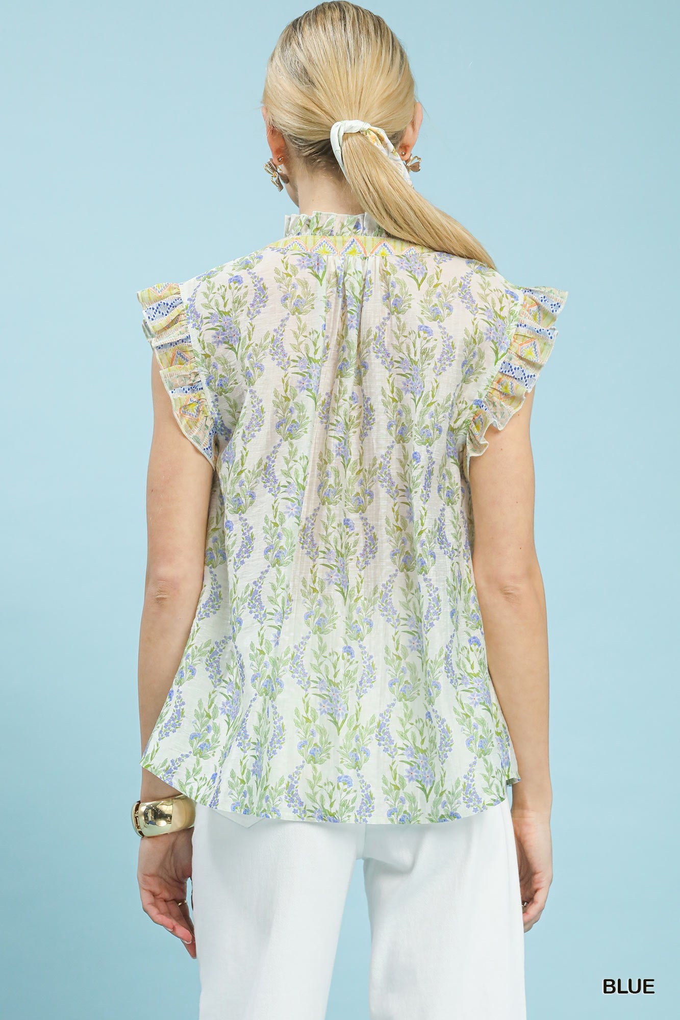 Woman wearing a floral blouse with ruffled sleeves against a light blue background