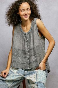 Woman wearing a sleeveless top and jeans sitting on a chair against a gray background